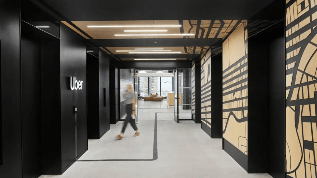 A hallway in Uber's office with a person walking past black walls featuring modern geometric designs. The company's logo is displayed on the left wall.