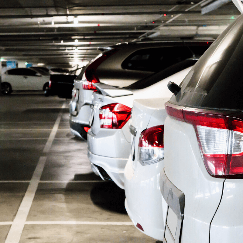 A row of parked cars in a dimly lit indoor parking garage, managed efficiently with advanced parking lot systems, viewed from the rear.