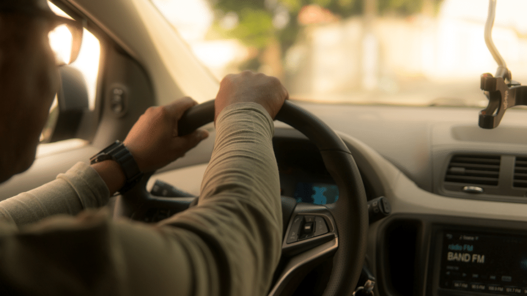 Close-up view of a person driving a car, with hands on the steering wheel. The car's dashboard displays the time and a radio station, hinting at advanced parking management systems integrated for effortless commercial parking.
