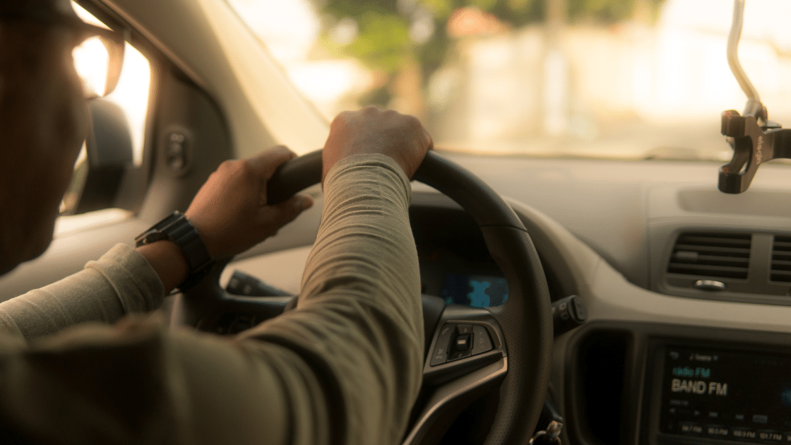 Close-up view of a person driving a car, with hands on the steering wheel. The car's dashboard displays the time and a radio station, hinting at advanced parking management systems integrated for effortless commercial parking.
