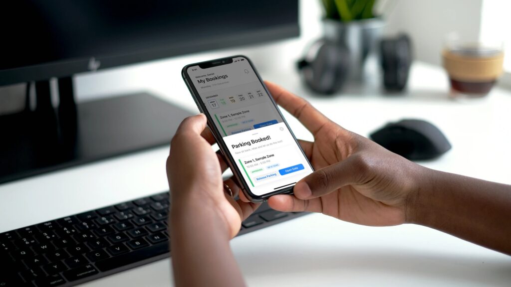 Person holding a smartphone displaying a Wayleadr booking confirmation screen, with a computer keyboard and monitor visible in the background.