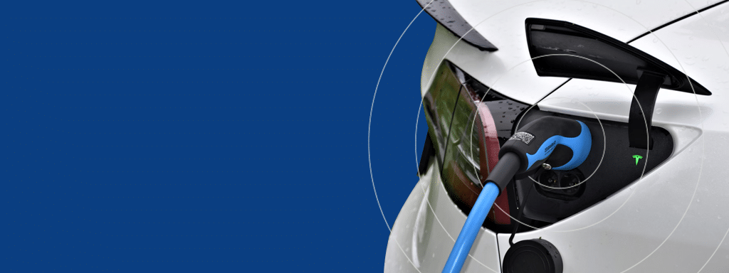 A close-up of an electric vehicle being charged, showing a blue charging cable plugged into the car's charging port in a commercial parking lot. The car's rear light is partially visible against a solid blue background.