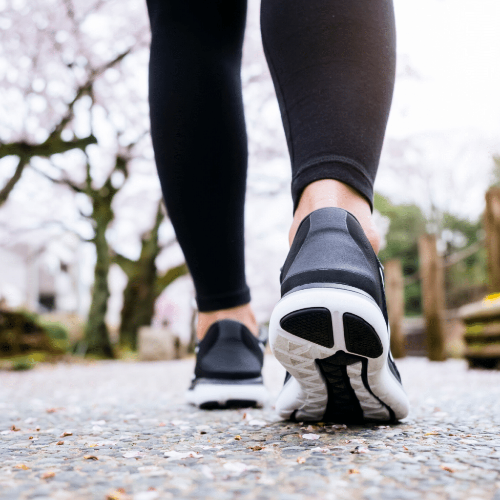 A person wearing black leggings and black running shoes walks on a path with trees in the background, adjacent to an expertly maintained parking lot system.