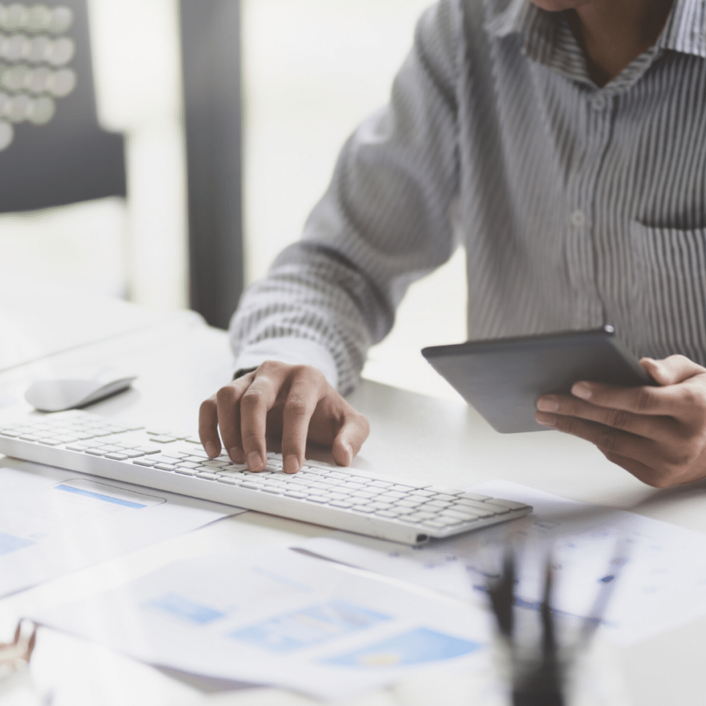 Person in a striped shirt using a tablet and typing on a keyboard at a desk with papers, a computer mouse nearby, and wayleadr software for parking lot management open on the screen.