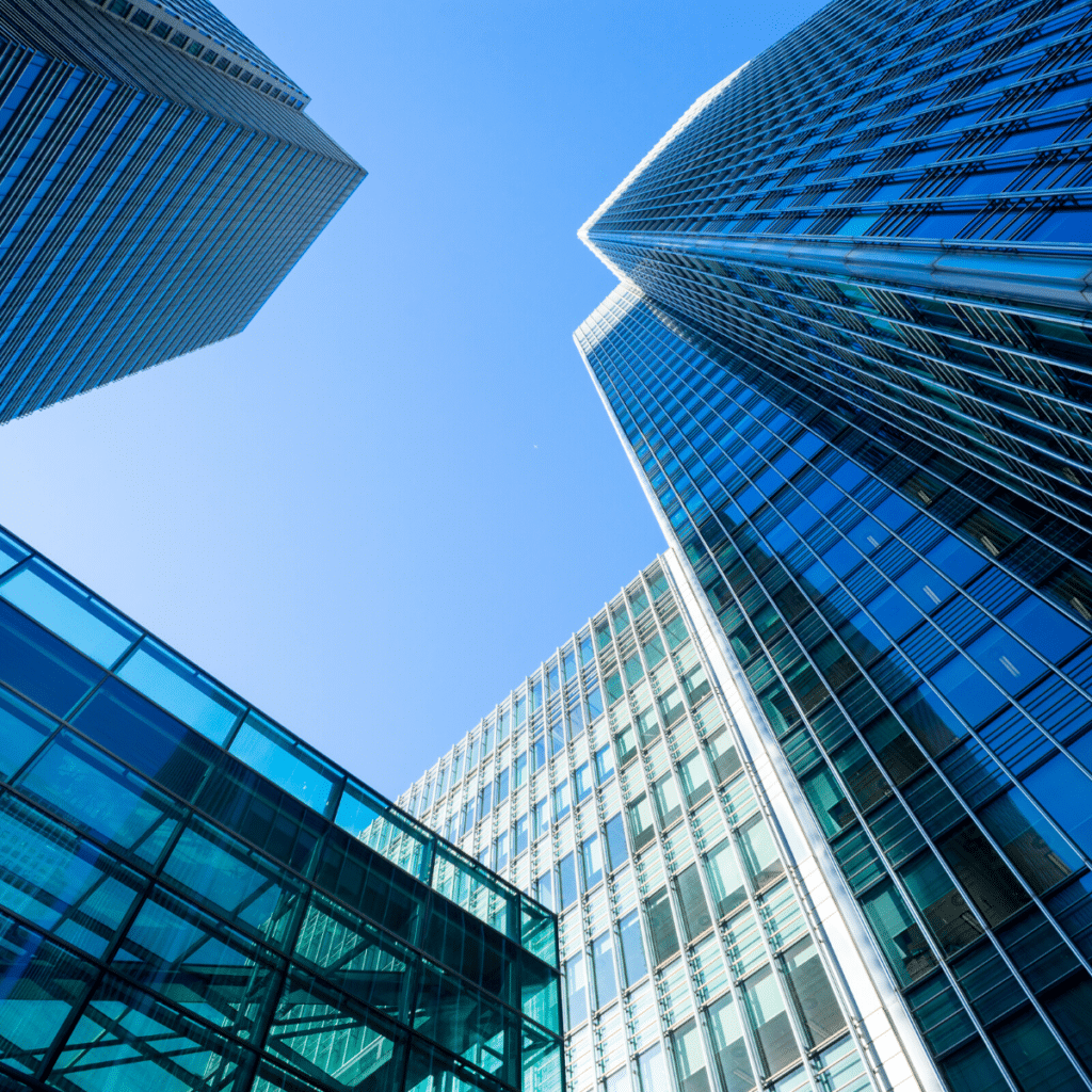 Upward view of modern glass and steel skyscrapers against a clear blue sky, with streamlined visitor parking areas seamlessly integrated into the design.