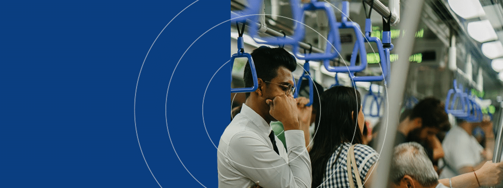 Commuters standing and holding onto blue handrails inside a crowded train, their minds often drifting to the hassle of parking management waiting on the other end of their journey.