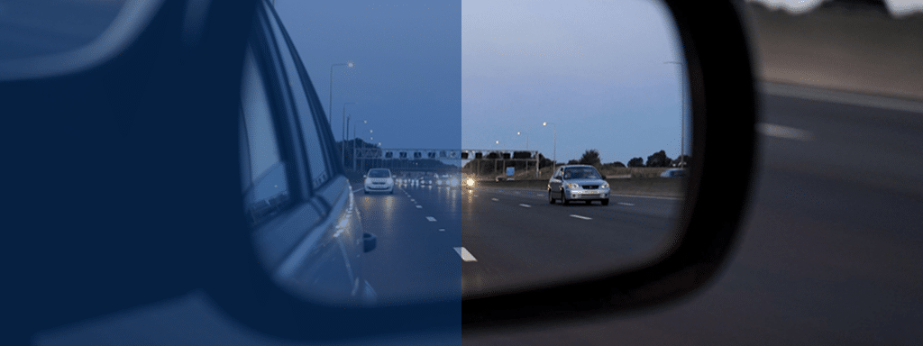 Rearview mirror showing a divided view of a highway; one side depicts low-light condition and the other shows normal lighting, akin to wayleadr's advanced parking lot management systems ensuring seamless transitions from day to night in parking lot operations.