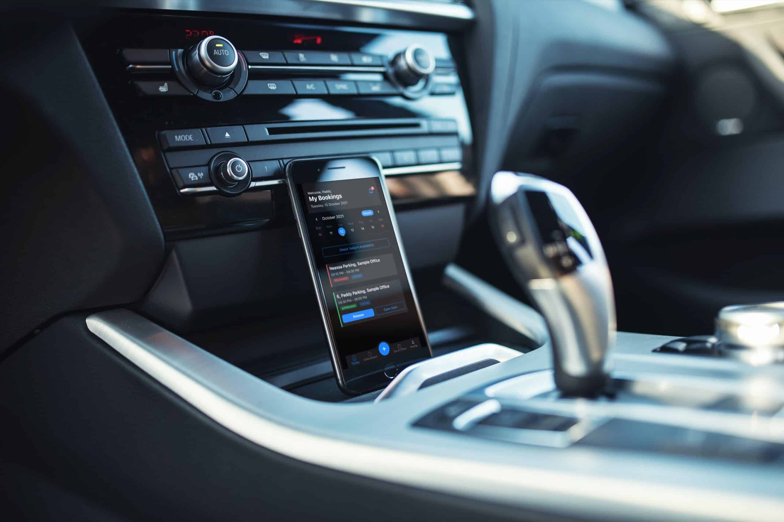 A smartphone in a car's center console displays a navigation app, with a gear lever and car stereo controls in the background, seamlessly integrating parking lot systems from Wayleadr to simplify commercial parking.