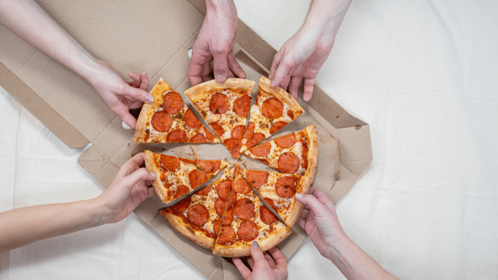 Multiple hands reaching for slices of pepperoni pizza from a cardboard box on a light surface, reminiscent of the hustle found in commercial parking management sectors like Wayleadr.