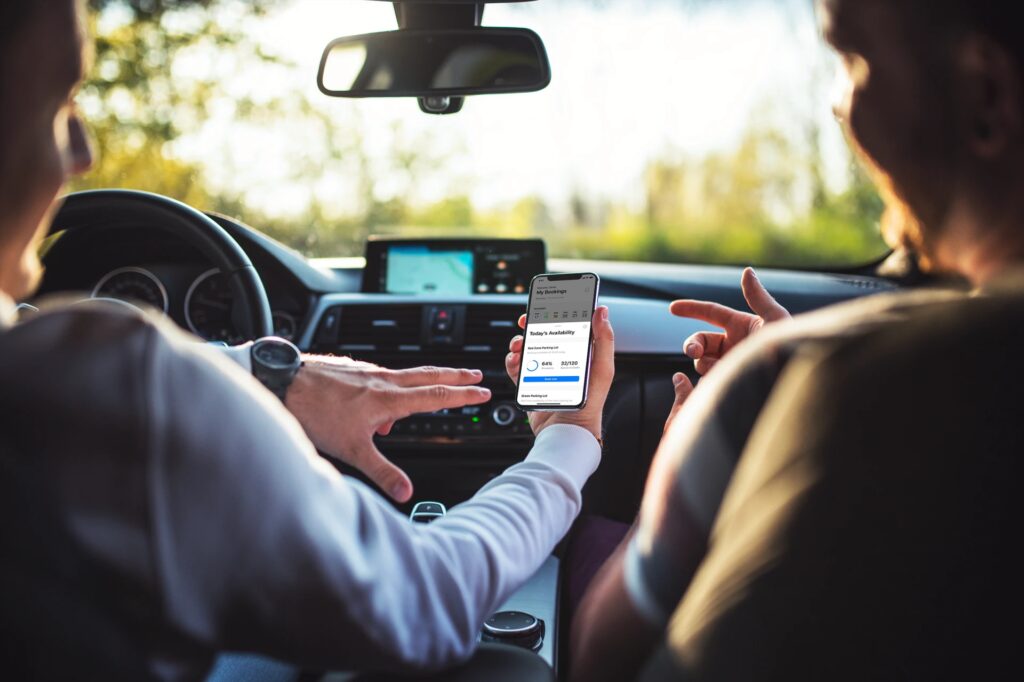 Two people sit in a car, one holding a smartphone displaying a ride-sharing app while the other points towards the screen. A GPS navigation system is visible on the car's dashboard, seamlessly integrating with advanced parking lot management for ultimate convenience.