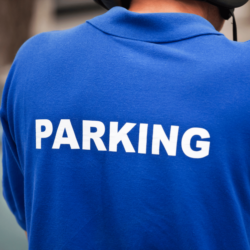 A person wearing a blue shirt with the word "PARKING" printed in white on the back, likely part of parking lot management.