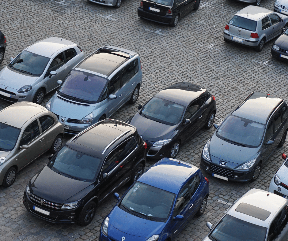 A parking lot equipped with advanced parking management systems, filled with various cars including sedans, a minivan, and an SUV, all arranged in lined rows on a stone-paved surface.