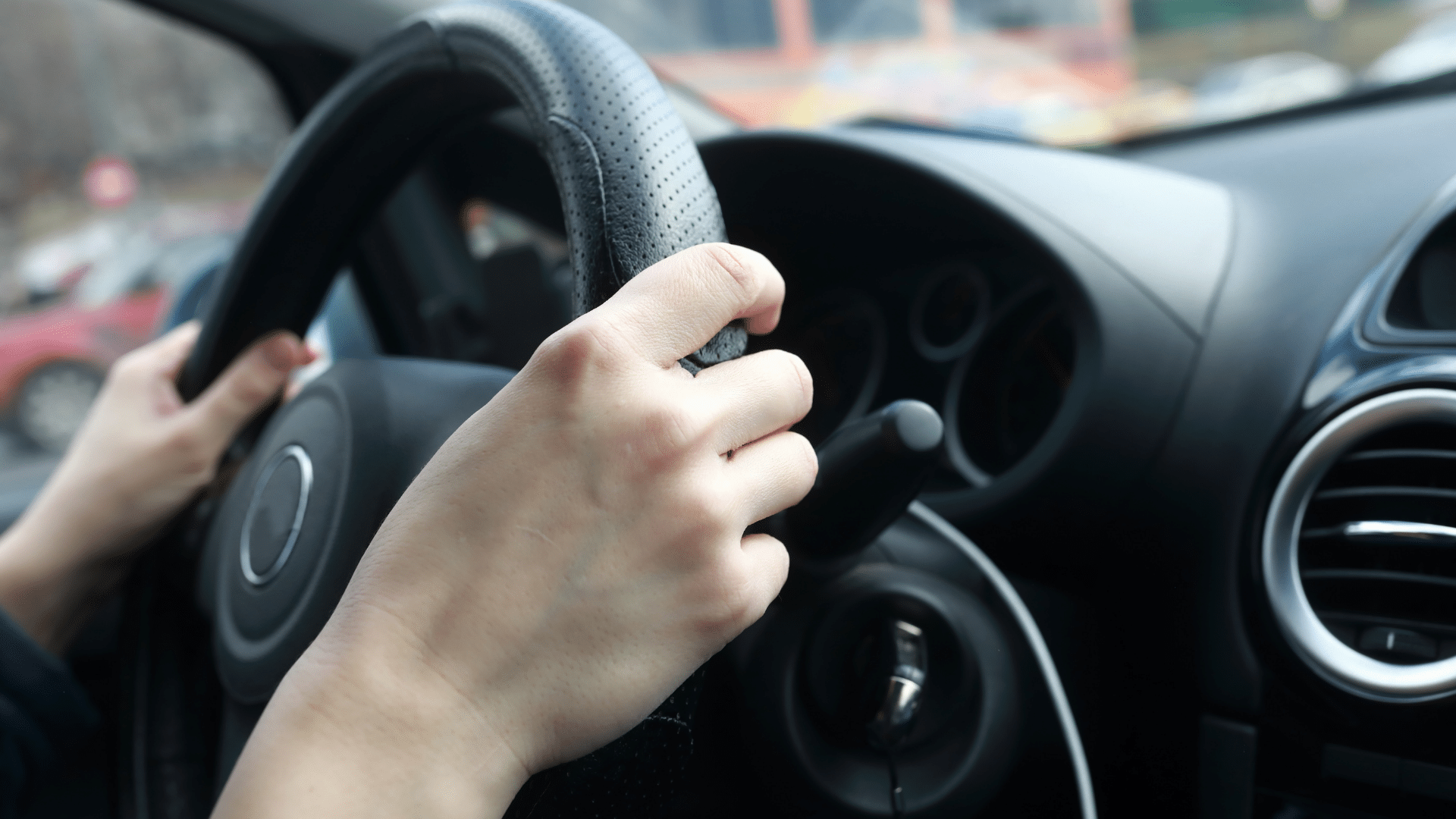 A person’s hands holding a steering wheel inside a car, with the dashboard and ignition key visible in the background, perhaps navigating through a parking lot system or integrating Wayleadr for efficient parking management.