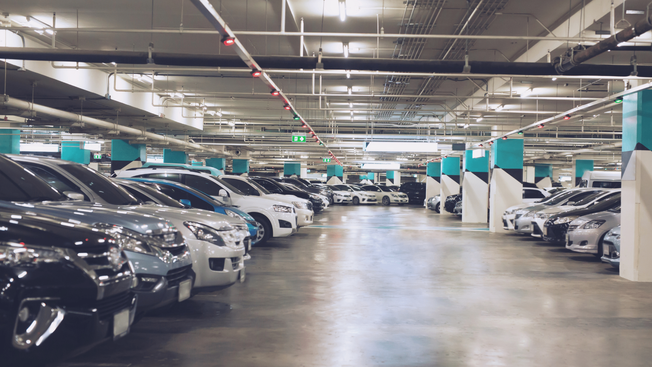 A well-lit underground parking garage with cars parked in organized rows on either side of a central aisle, featuring designated visitor parking managed efficiently.