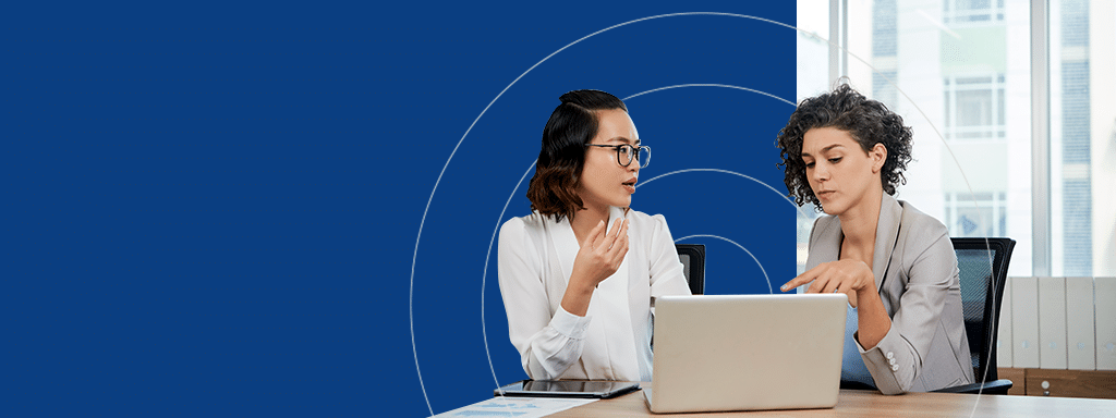 Two women, seated at a desk with a laptop, engage in a discussion about parking management. The background is blue with a partial circular design and a window showing a building.