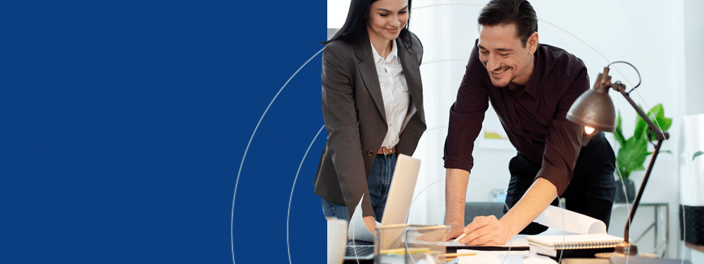 Two colleagues, a woman in a gray blazer and a man in a maroon shirt, collaborate on a project at a desk with documents and a laptop in an office space, brainstorming innovative parking lot systems by Wayleadr.