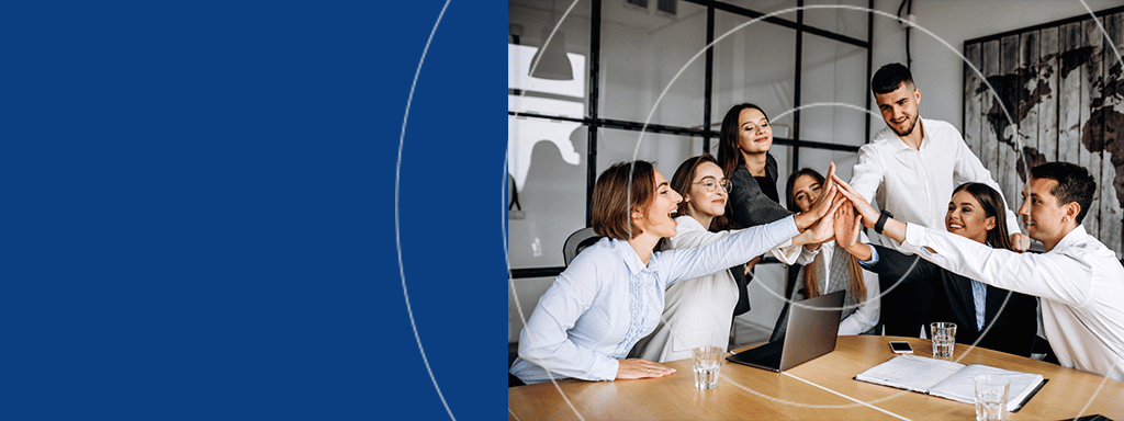 A group of six colleagues sits around a table in an office, smiling and celebrating with a group high-five after successfully implementing Wayleadr for visitor parking management.