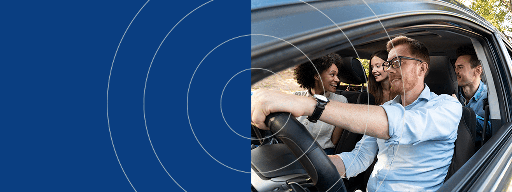 A person is driving a car with three passengers, all smiling and engaged in conversation about parking lot management.