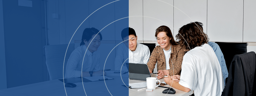 Three people sit around a table, collaborating while looking at a laptop. One person is taking notes, while another is typing. An office environment focused on commercial parking management systems is visible in the background.