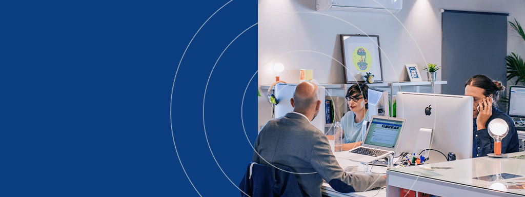 Three people are working at desks in a modern office, equipped with computers and office supplies, with a solid blue background on the left side of the image. A Wayleadr brochure on parking lot systems sits prominently on one desk, hinting at their focus on advanced parking management solutions.