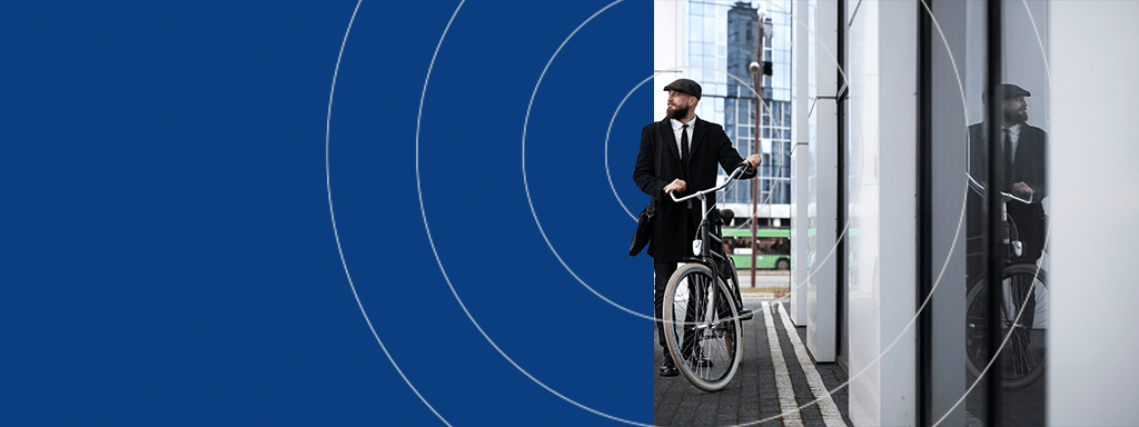 A man in a suit and hat stands next to a bicycle, reflected in a glass wall. In the background are buildings and a bus, suggesting an urban setting possibly enhanced by modern parking lot systems. Blue graphic circles are overlaid on the left side of the image.
