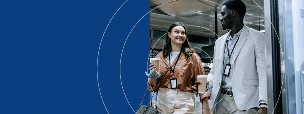 Two people walking and talking, holding coffee cups and wearing work badges around their necks, stroll past the visitor parking area, discussing the latest updates from Wayleadr on parking lot management.