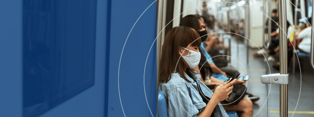 People sitting in a subway train wearing face masks. A woman in focus is using her smartphone, possibly checking updates on parking lot systems for more efficient commercial parking.