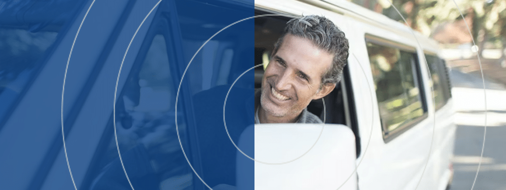 A smiling man with graying hair looks out the driver's side window of a white vehicle. The left side of the image features a blue overlay with circular graphic elements, hinting at convenient visitor parking options.