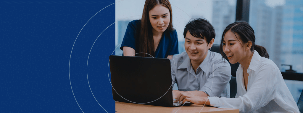 Three people are looking at a laptop screen together, deeply engaged in a discussion about parking lot management. They are seated at a wooden table with a cityscape visible through the window in the background.