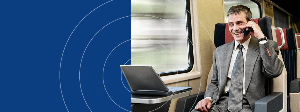 A man in a suit talks on a mobile phone while working on a laptop aboard a train, discussing wayleadr and efficient parking lot management.