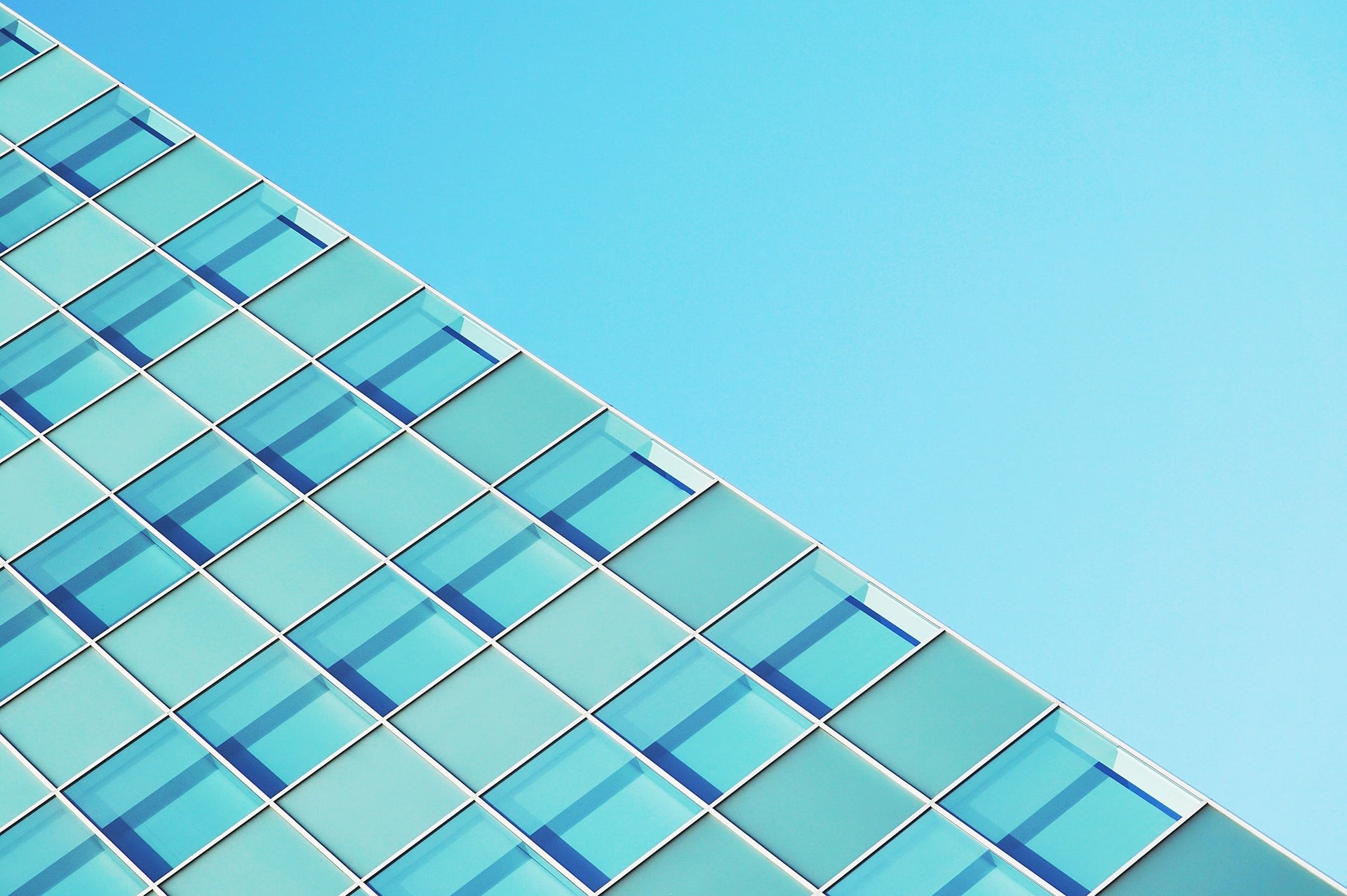 A section of a modern glass building with blue-tinted windows set against a clear blue sky, conveniently located near visitor parking.
