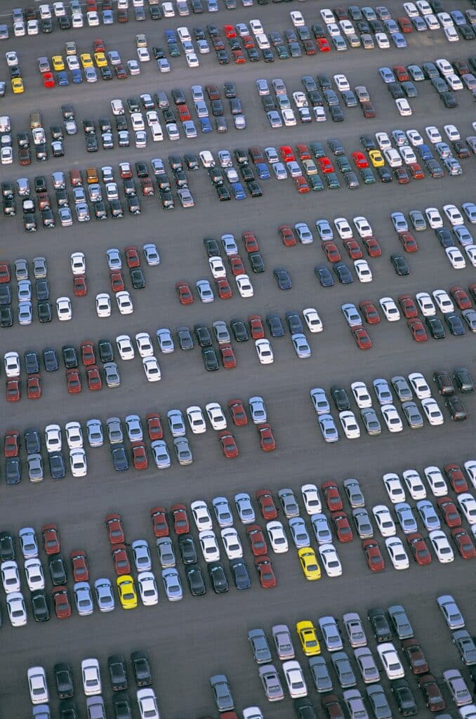 Aerial view of a large commercial parking lot with rows of parked cars in varying colors and sizes.