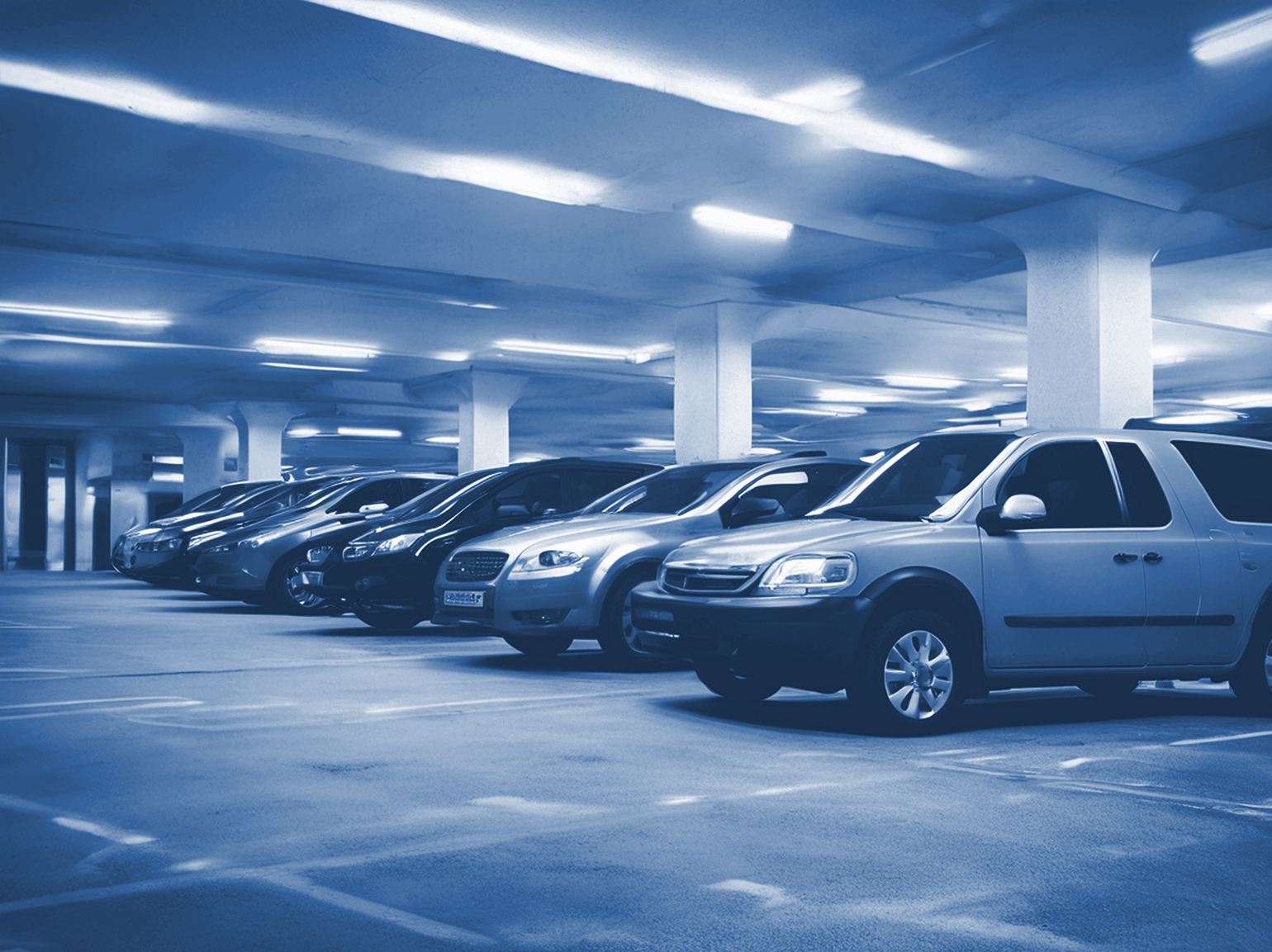 A row of parked cars in a dimly lit underground parking garage with concrete pillars and overhead lighting showcases the efficiency of professional parking management.