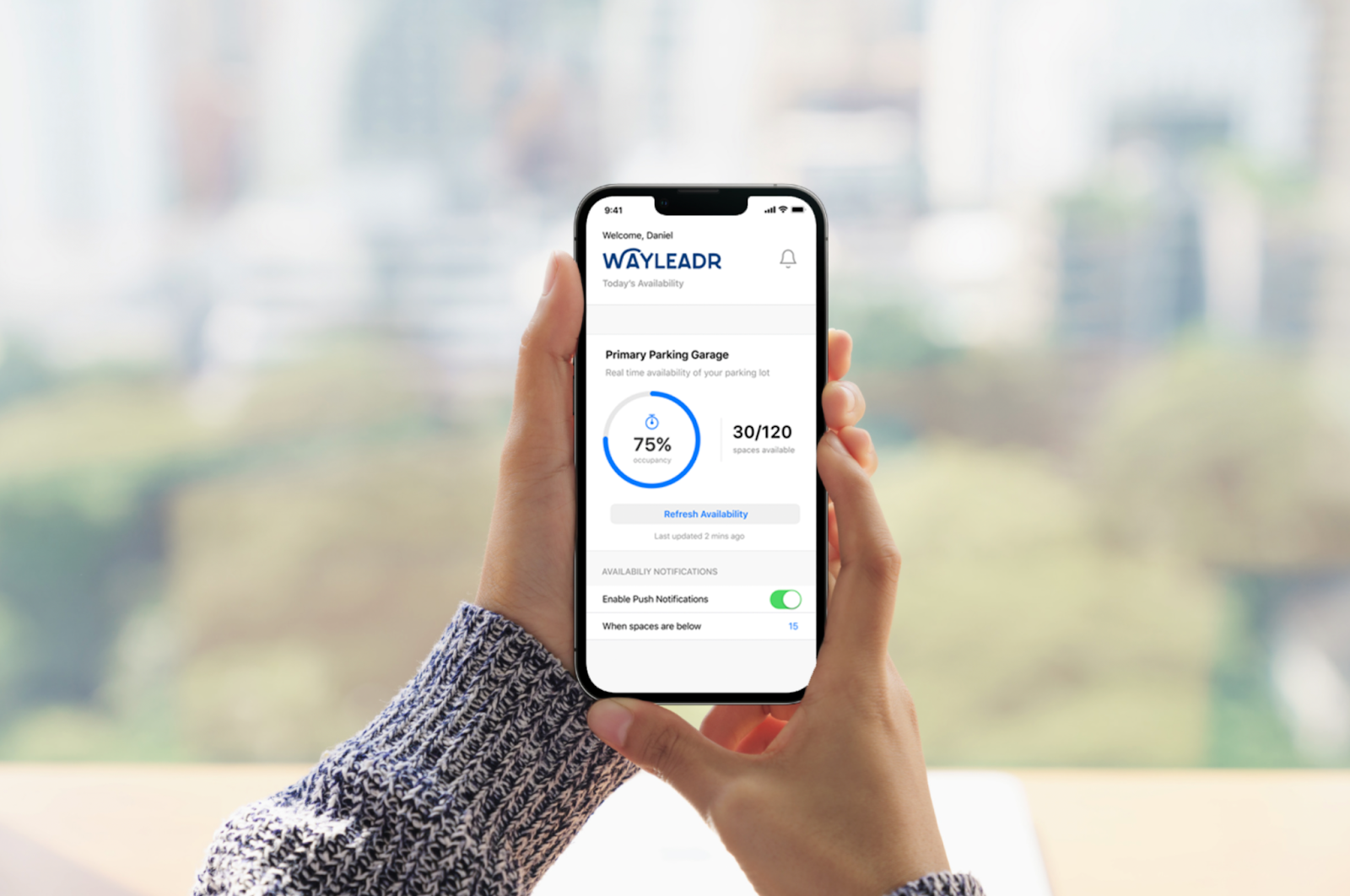 Person holding a smartphone displaying a parking app with 75% garage occupancy and notifications enabled.