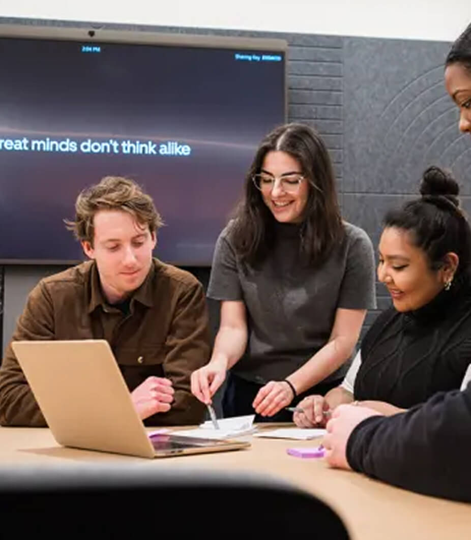 Four people collaborate around a table with a laptop and papers; a screen behind them displays the text, "Great minds don't think alike.