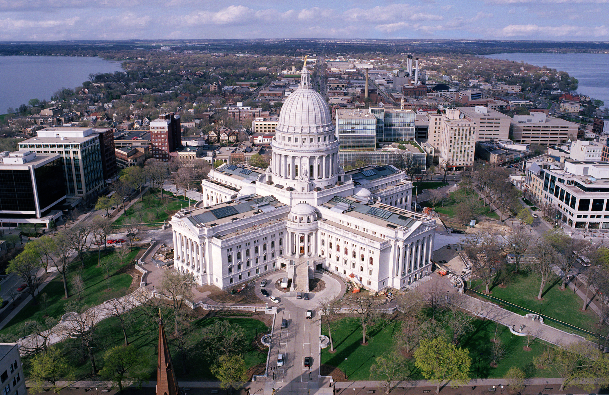 Aerial view of the Wisconsin State Capitol building in Madison, surrounded by city buildings, streets, and lakes in the background.