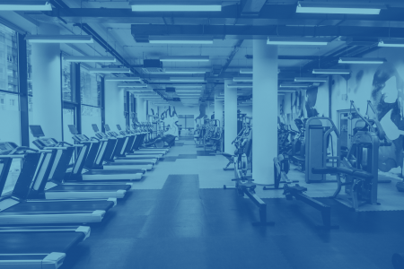 A spacious indoor gym with multiple treadmills, exercise bikes, and strength training equipment lined up neatly under bright fluorescent lighting.