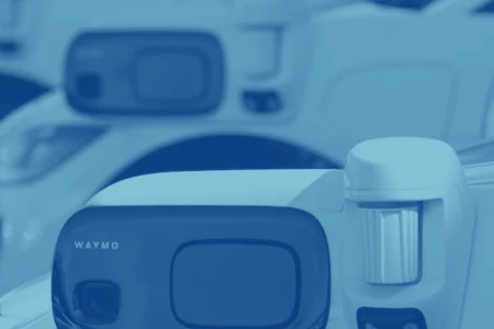 Close-up view of a row of Waymo self-driving cars equipped with various sensors and cameras, lined up in the visitor parking area. The white vehicles prominently display the Waymo logo, seamlessly integrating with advanced parking lot systems like Wayleadr.